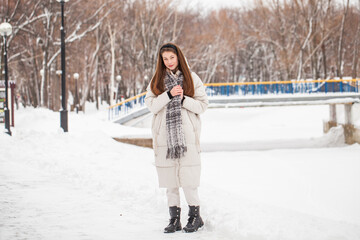 Young beautiful woman in a gray down jacket in a winter snowy park