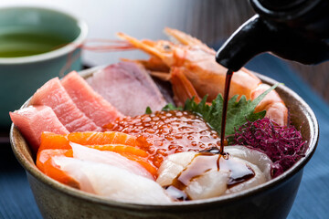 食卓に配膳された海鮮丼に醤油をかける