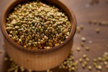 Unprocessed green buckwheat in a wooden bowl on a wooden board.
