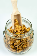 Glass jar full of peeled walnuts with wooden stick to catch them, isolated white background.