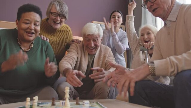 Ethnically diverse group of seniors throwing dice while playing tabletop game at nursing home