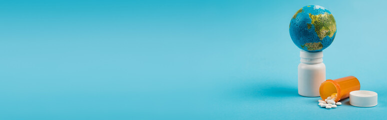 Small globe on jar with pills from new omicron strain on blue background with copy space, banner.