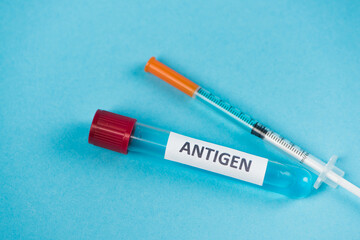 Close up view of syringe and test tube with antigen lettering on blue background.