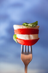 Vertical close up view of a caprese salad over a fork with blue hour and dramatic cloud as background