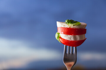 Caprese salad over a fork with blue hour and dramatic cloud as background