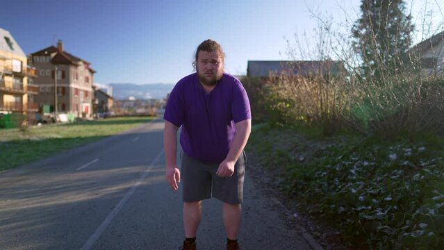 Determined chubby young man running outdoors. Motivational lifestyle concept of overweight fat person runner exercising. Tracking shot
