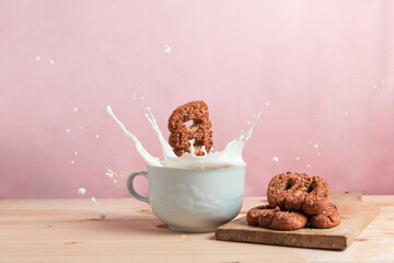 Biscuit falling into a milk cup with milk splash over a wooden table and pink background