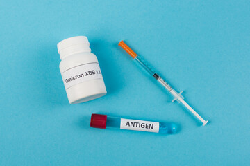 Top view of antigen near pills with omicron xbb lettering and syringe on blue background.
