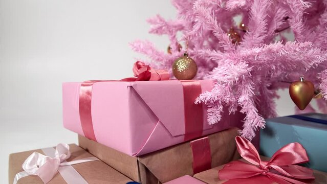 Still life of wrapped and tied with ribbon present boxes put under decorated pink Christmas fir. Isolated closeup view of New Year composition of pine ornated with golden toys and gifts under it