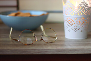 Glasses, bowl of biscuits, lit candles and books in the background. Selective focus.