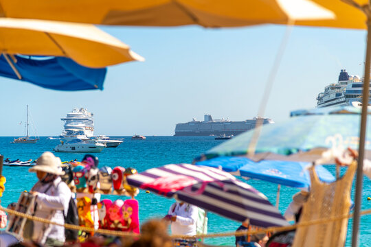 Cruise ships, jet skis, sailboats, yachts and motorboats can be seen at sea through a colorful beachfront scene along the coast of Cabo San Lucas, Mexico. - Powered by Adobe