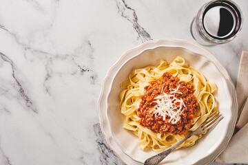 A plate of tagliatelle pasta with BOLOGNESE SAUCE and a glass of red wine on a light marble background. Top view. Copy space.