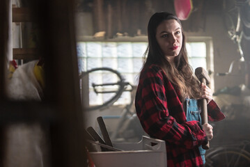 Woman in a garage holding a big hammer. 