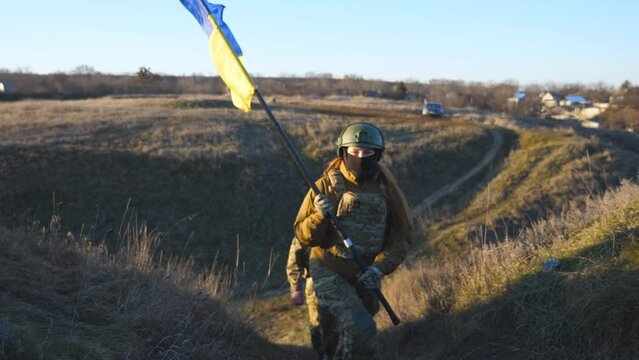Soldiers of ukrainian army walks at hill top to lifted up flag of Ukraine. People in military uniform waving national yellow-blue flag against blue sky as sign of victory against russian aggression
