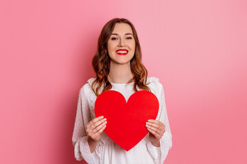 smiling positive girl holding big red heart with copy space for text isolated on pink background