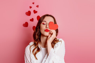 woman closes one eye with a heart and sends an air kiss isolated on pink background