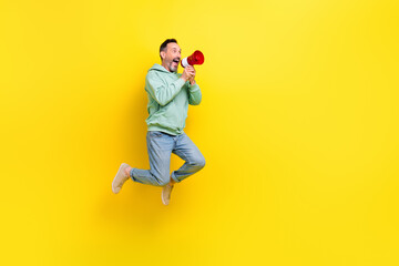 Fototapeta na wymiar Full length photo of cool excited man wear green sweatshirt telling toa announcement empty space jumping high isolated yellow color background