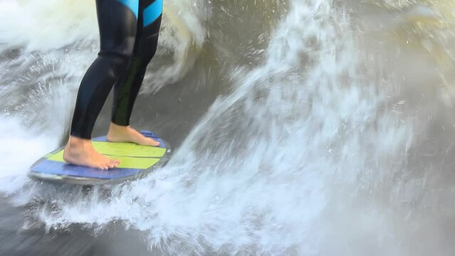 Sportsman dressed in neoprene swimsuit wakesurfs performing stunts at high speed standing on colorful board among foamy waves closeup
