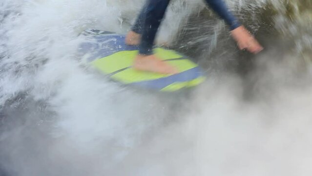 Man rider wearing neoprene swimsuit wakesurfs at high speed touching water with hand standing on board among foamy waves closeup