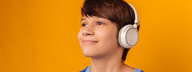 Banner size cropped photo of a smiling teen boy wearing wireless headphones over yellow background.