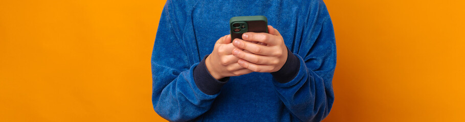 Crop banner size faceless photo of some male kid hands using a smart phone over yellow background.