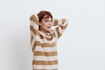 horizontal photo on a light background of a pleasant, beautiful, attractive woman straightening her hair standing in a stylish striped sweater sideways to the camera