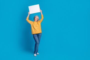 Full size photo of cheerful aged lady hands hold empty space ad blank isolated on blue color background