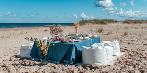 Delicious food and flowers for outdoor summer picnic. Lunch on the beach by the sea. Picnic in the style of boho.