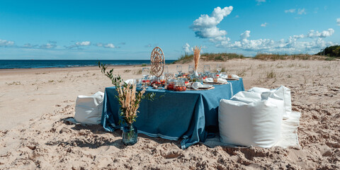 Fototapeta na wymiar Prepared surprise on the beach by the sea. Delicious food and flowers for outdoor summer picnic. Picnic in the style of boho. Panorama.