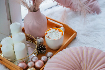 Mug of coffee with marshmallows on a wooden tray, white candles. Christmas decor element in pink color.