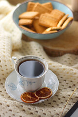Vintage books, reading glasses, e-reader, cup of tea, bowl of biscuits and lit candle on the table. Selective focus.