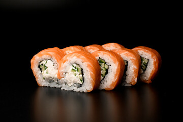Philadelphia sushi rolls with salmon, cucumber, avocado, cream cheese. On dark background.