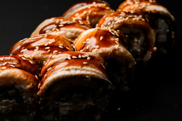 Close-up view of sushi rolls Philadelphia with smoked eel with soy sauce and sesame seeds on dark background.