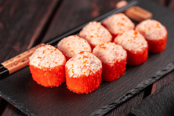 Sushi roll with mayonnaise sauce and red tobiko caviar served on black board and soy sauce.