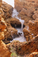 Fototapeta na wymiar Water running over rocks into a small pool at the Atlantic Ocean in Algarve, Portugal on a warm winter day.
