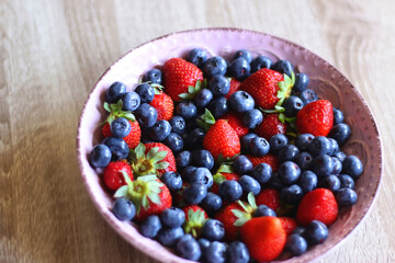 Pink rustic bowl filled with fresh blueberries and strawberries. Wooden background, selective focus.
