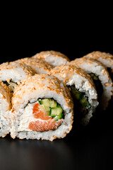 Close-up of sushi rolls california with smoked salmon, cream cheese, cucumber, sesame seeds on dark background.