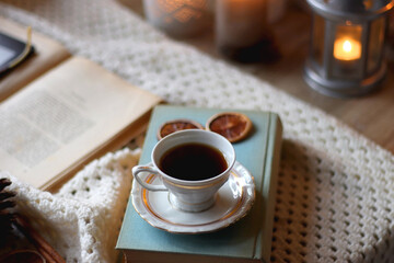 Cup of tea, books, tablet, bowl of cookies, various spices, pine cones and lit candles. Hygge at home. Selective focus.