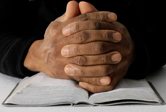 praying to God with hands on bible together with cross on grey black background with people stock photo