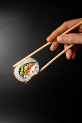 hand holding one piece of roll california with smoked salmon garnished sesame seeds with bamboo chopsticks