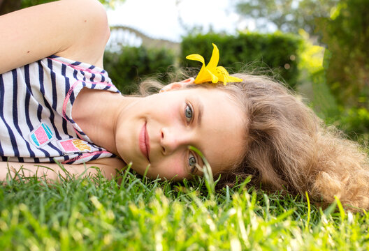 face portrait of a smiling teenage girl 12 years old lying on grass on sunny day. enjoyment of nature outdoors, relaxation, dreams. Hello summer, spring, sunbathing. happy childhood