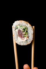 Close-up of roll california with salmon garnished sesame seeds in bamboo chopsticks