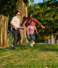 Fototapeta premium lesbian female couple. playing, running and having fun with their adopted son in the park, real people, green background, copy space.