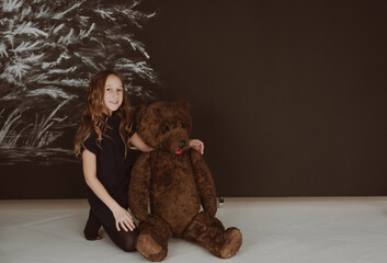 The girl is holding a large trading bear in her hands. Gift bear on a black background. The tree was drawn with crayons.