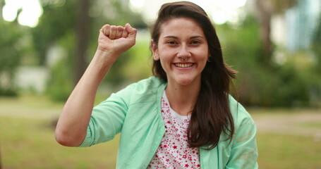 Strong young woman raising fist in the air smiling to camera