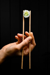 female hand holds kappa maki sushi roll with cucumbers and rice wrapped in nori with with chopsticks © fesenko