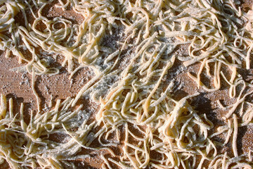 Uncooked homemade noodle with flour on wooden cutting board. Cooking. Top view.
