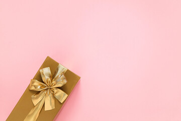 Golden gift box with golden ribbon and bow on a pink background. Top view. Copy space.