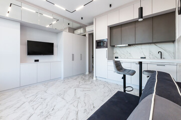 The interior of the kitchen and living room in light white colors with a table, chairs and a TV in a large free space.