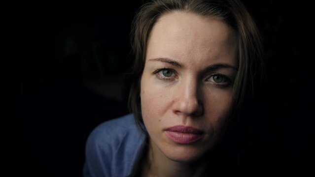 A beautiful woman looks up and looks into the camera with a serious expression. A close-up portrait of a Girl with a tired or sad look on a black background. Dramatic cinematic female portrait.